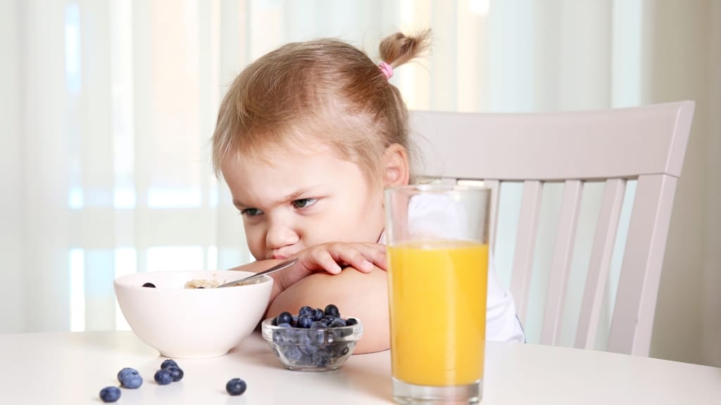 Picky Eater sitzt vor Schale mit Blaubeeren und Orangensaft